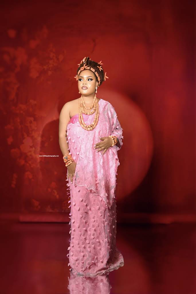 A woman in elegant pink traditional attire photographed against a rich red studio backdrop by FAITHFYN PHOTOGRAPHY